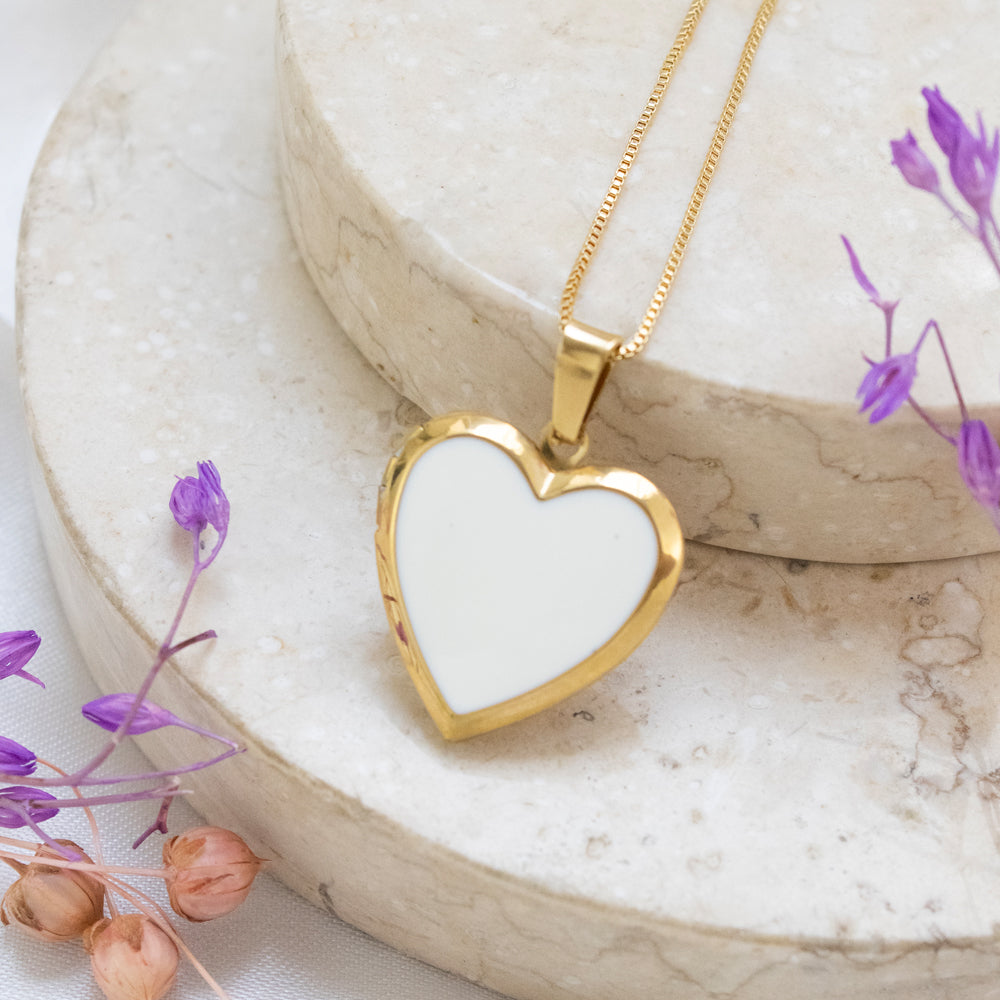 Collar relicario en forma de corazón con interior blanco, para colocar fotos dentro de el. Collar en tono dorado/acero